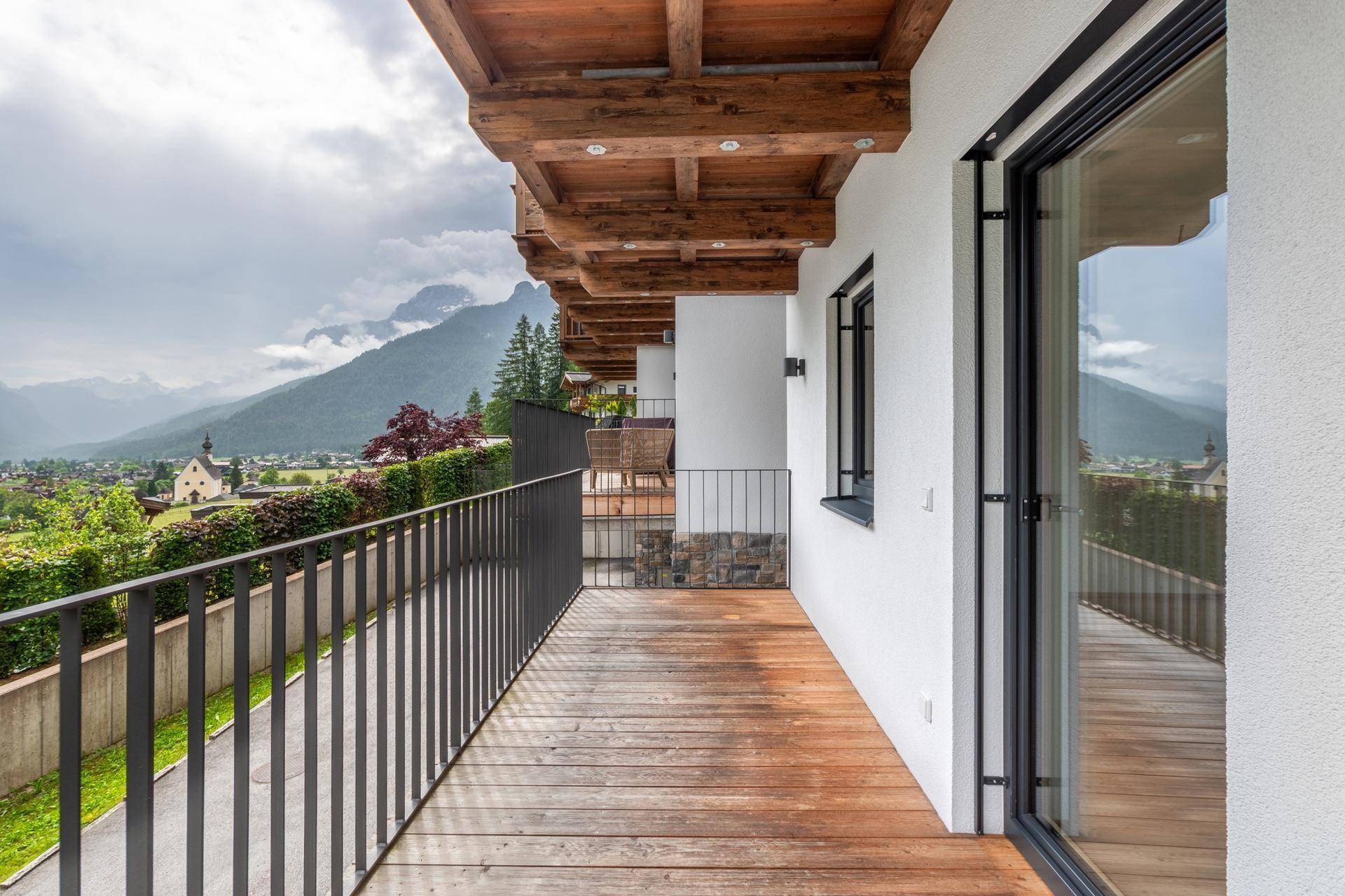 Langer Balkon mit Holzboden und modernem Geländer, bietet einen weiten Blick auf die Berge und das Tal.