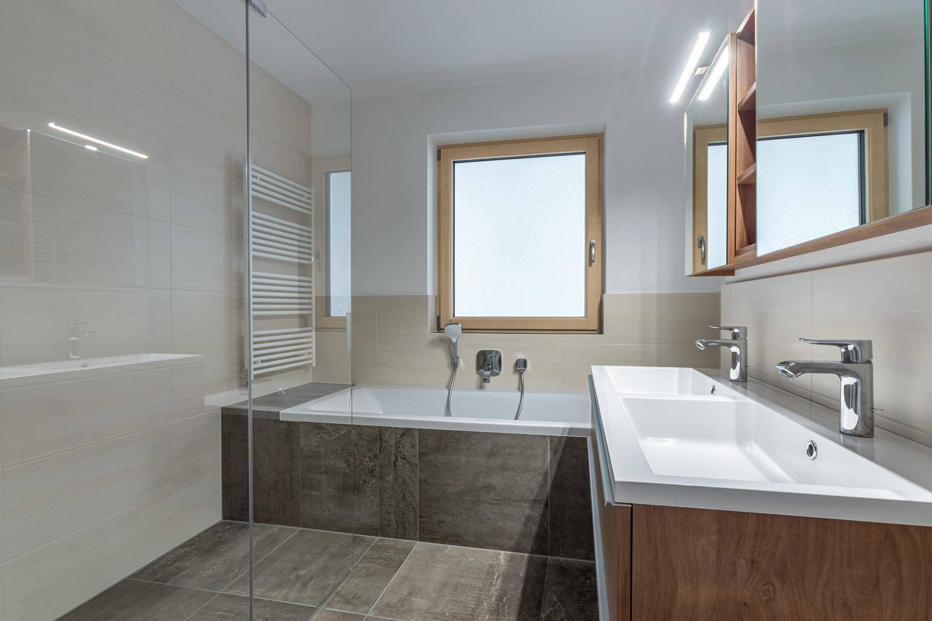 Modernes Badezimmer mit Doppelwaschbecken, Badewanne und beheiztem Handtuchhalter.