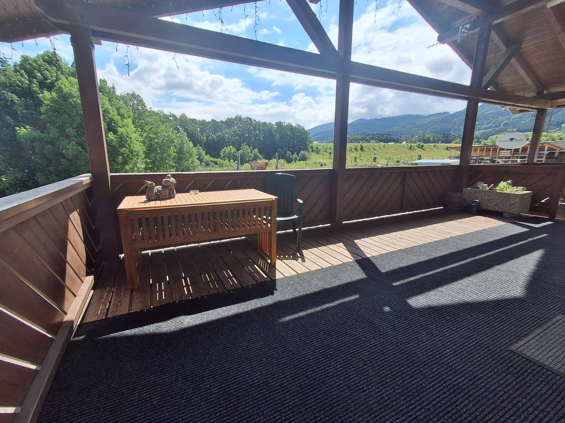Geräumiger überdachter Balkon mit Holzboden und Sitzbereich, bietet eine malerische Berglandschaft.