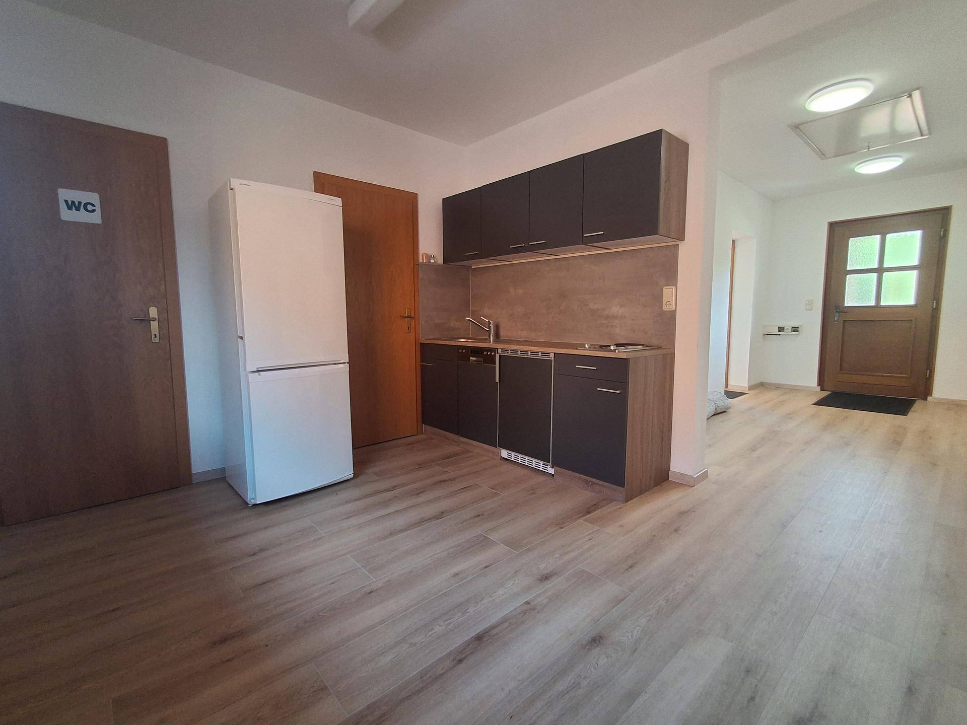 Kleine Küchenzeile mit dunklen Schränken und Kühlschrank, integriert in einen offenen Bereich.