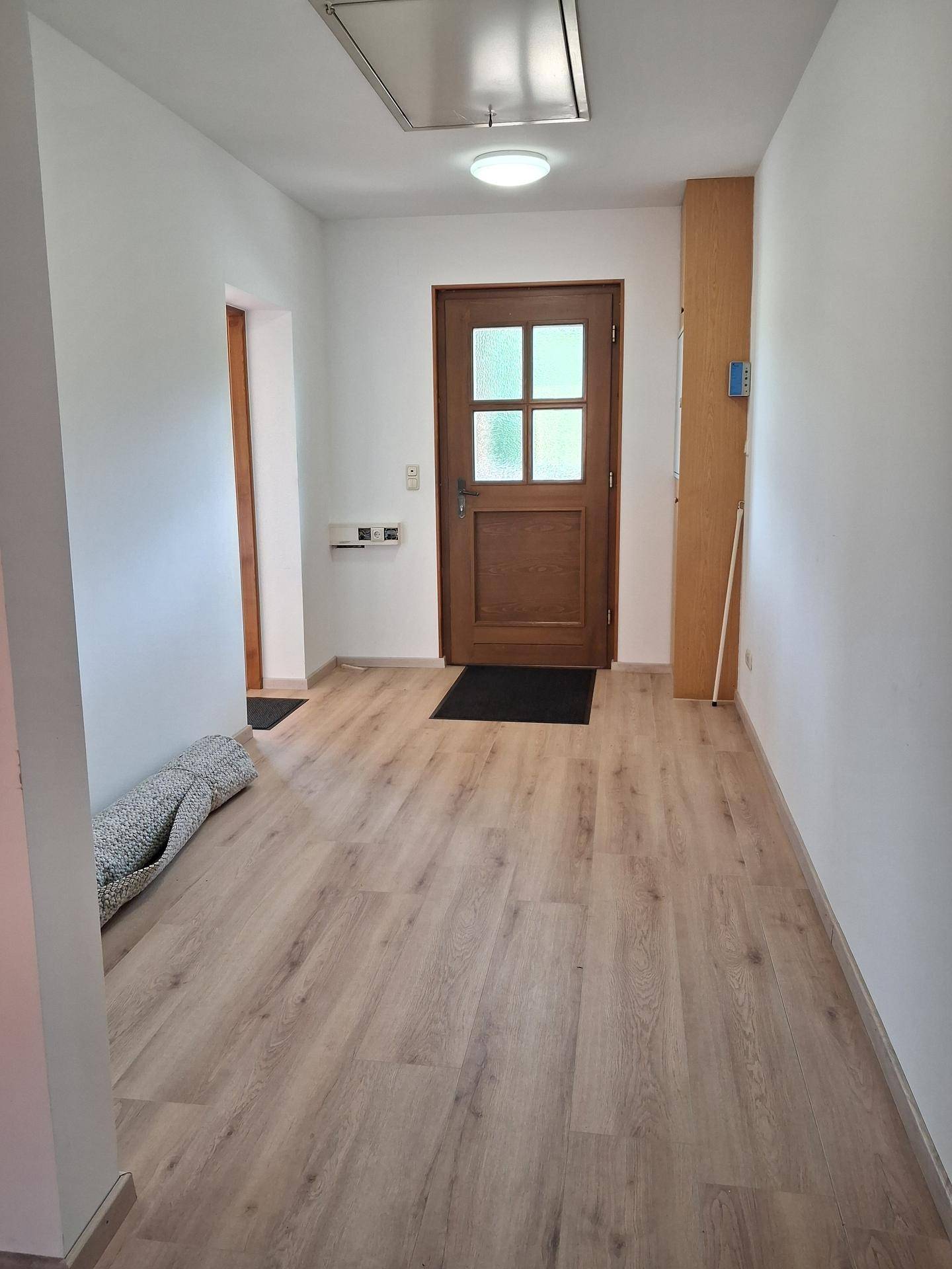 Heller Eingangsbereich mit Holztür und Laminatboden, führt zu weiteren Räumen im Gebäude.