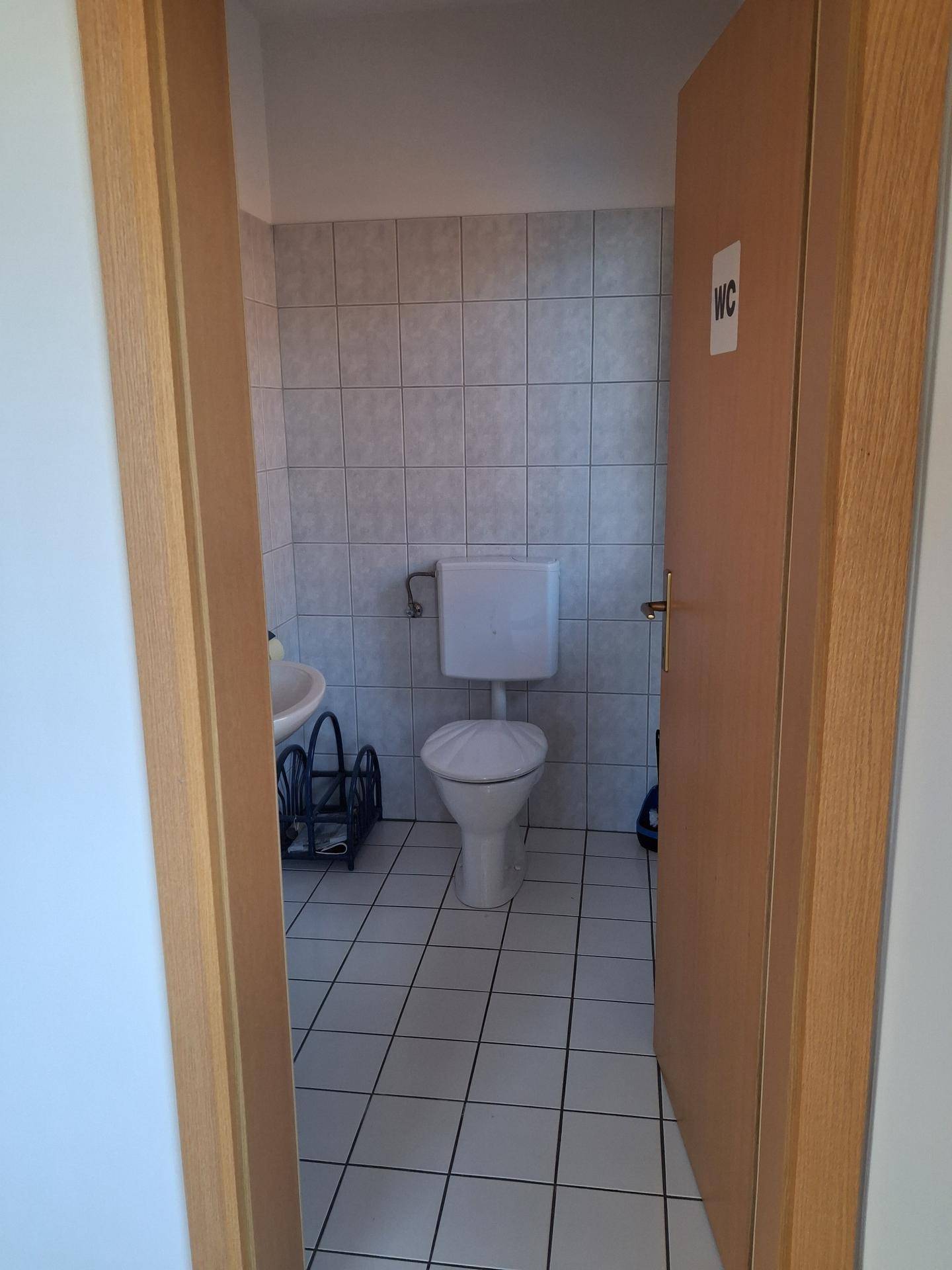 Einfache Gästetoilette mit Fliesenboden und Wandfliesen, ausgestattet mit einem WC und Waschbecken.