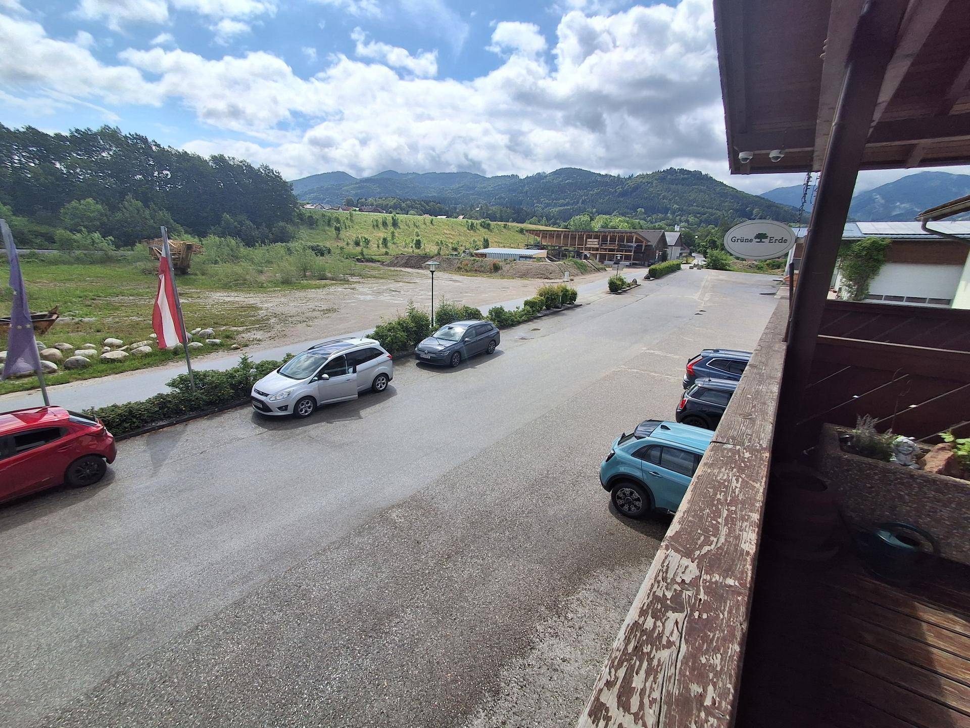 Weitläufige Außenansicht mit Parkplätzen und Gebäuden, umgeben von grüner Landschaft und Bergen.