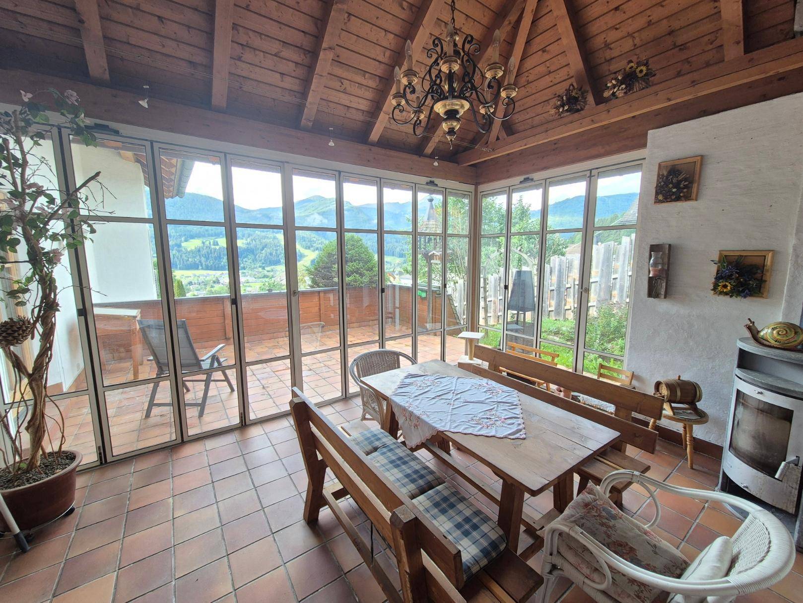 Heller Wintergarten mit Holzdach, Terracotta-Fliesen und Panoramablick auf die Berge.