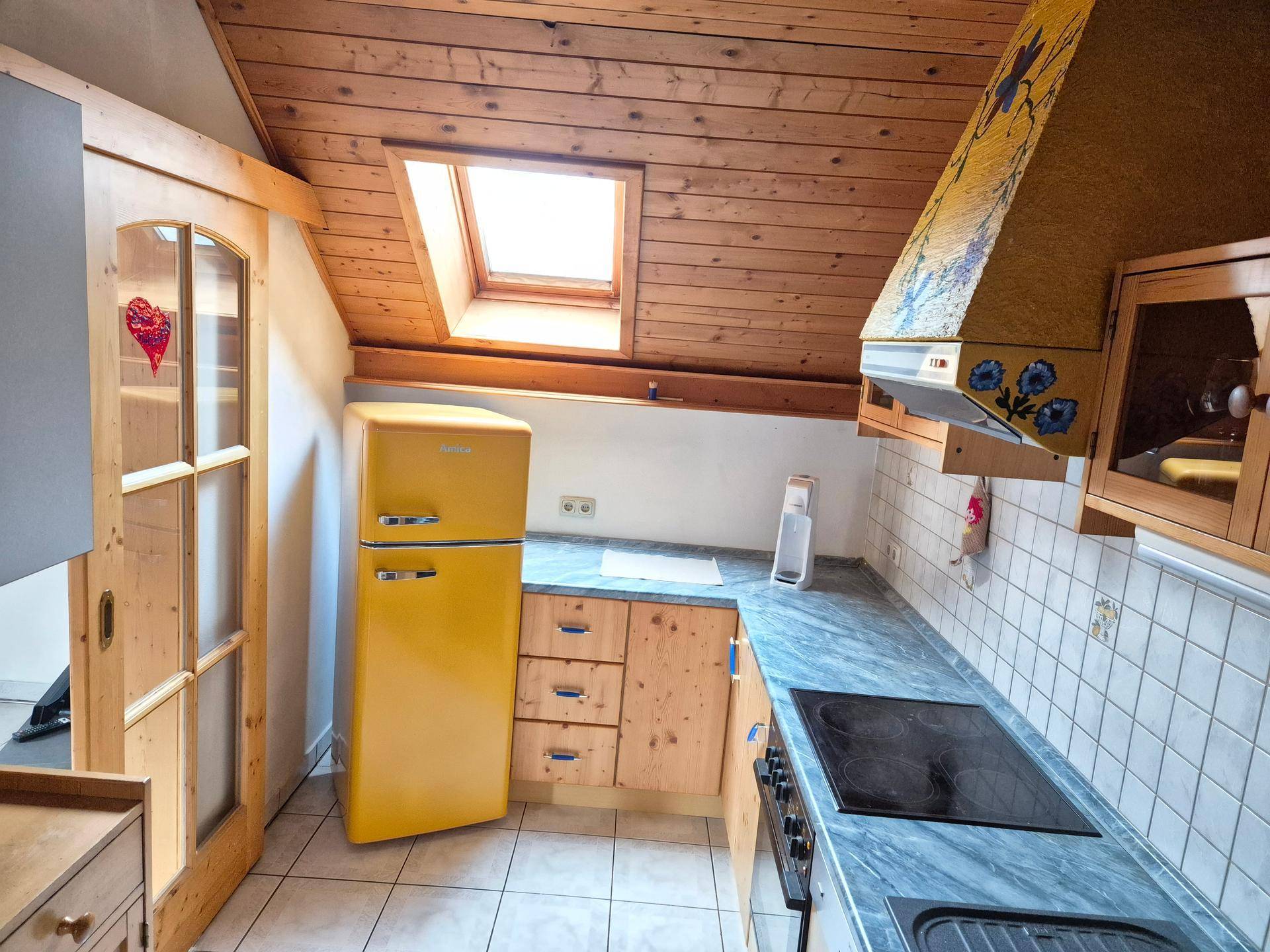 Helle Küche mit Holzschränken, Dachfenster und einem auffälligen gelben Kühlschrank.