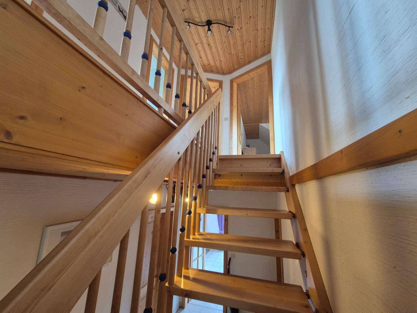 Holztreppe mit Geländer und Holzdecke, die zu den oberen Stockwerken führt.
