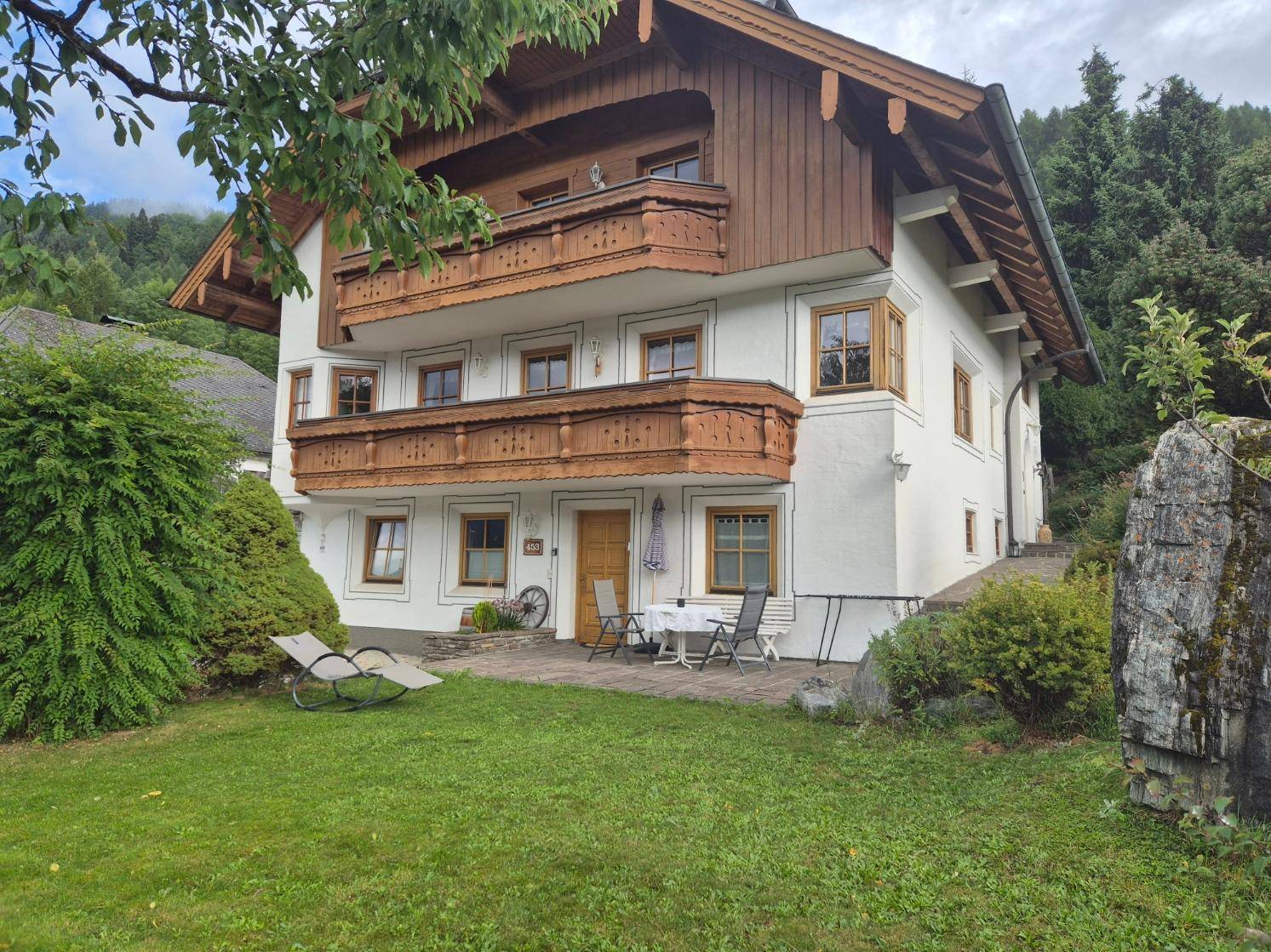 Traditionelles Haus mit Holzbalkonen, Garten und kleiner Terrasse im alpinen Stil.