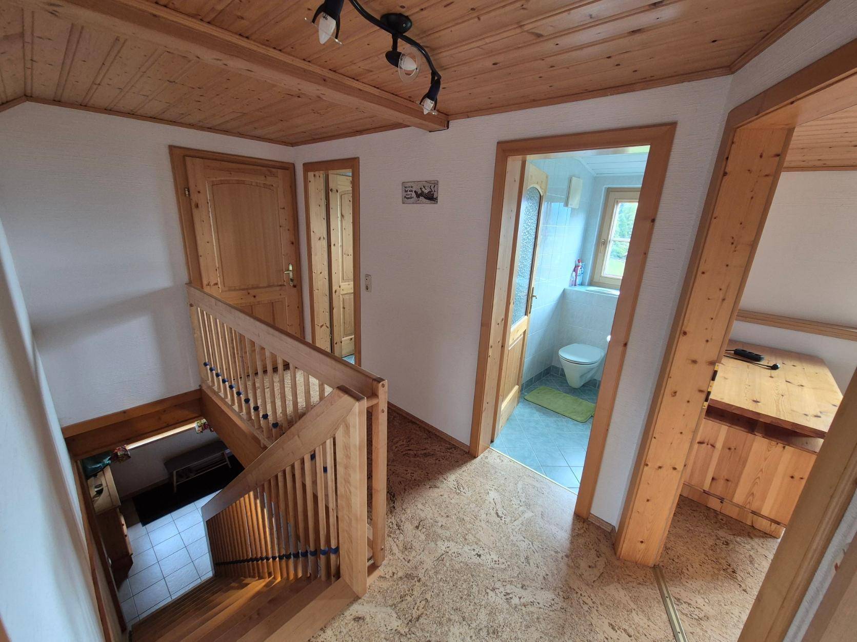Flur mit Holztreppe und Zugang zu einem Badezimmer, ausgestattet mit Korkboden.