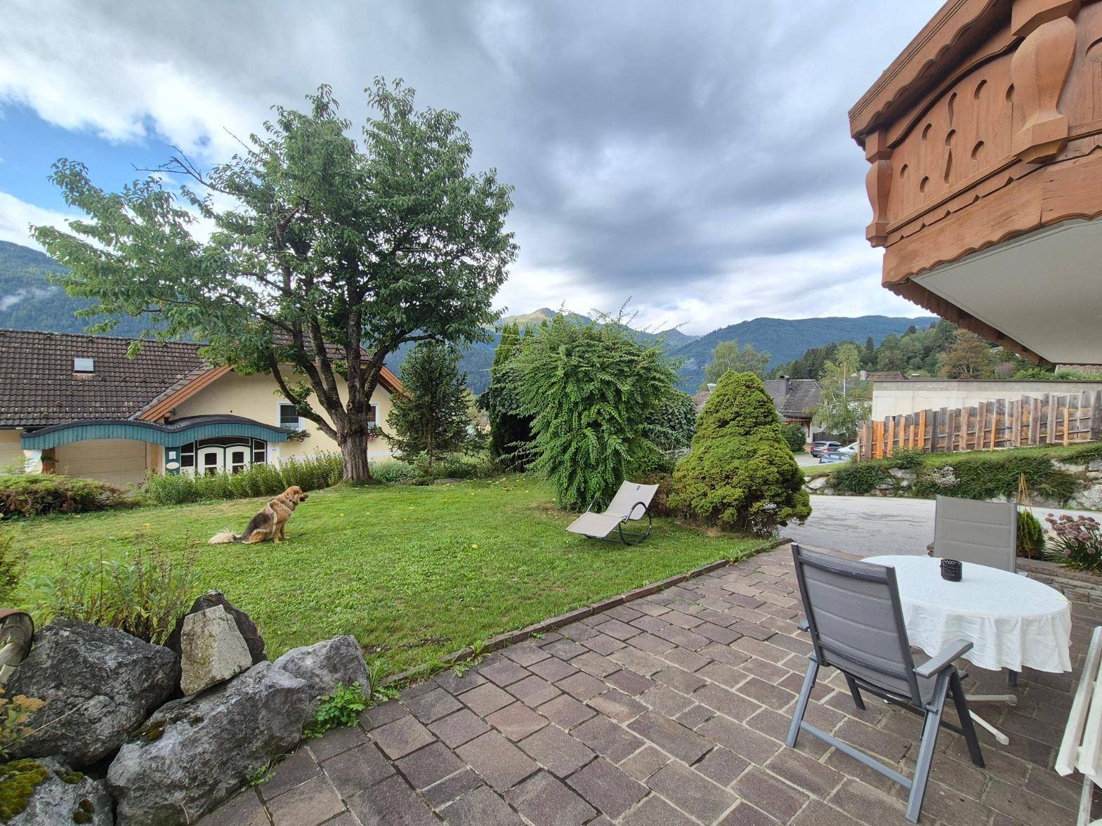 Geräumiger Garten mit Rasenfläche und gepflasterter Terrasse, umgeben von grüner Natur.