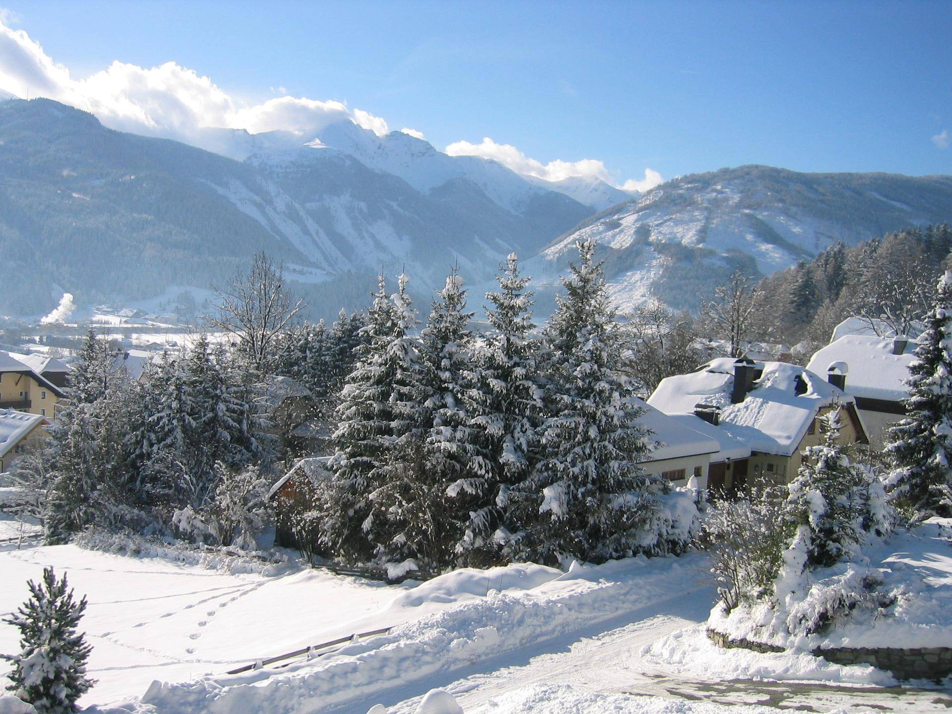 Malerische Winterlandschaft mit verschneiten Bäumen, Häusern und majestätischen Bergen.