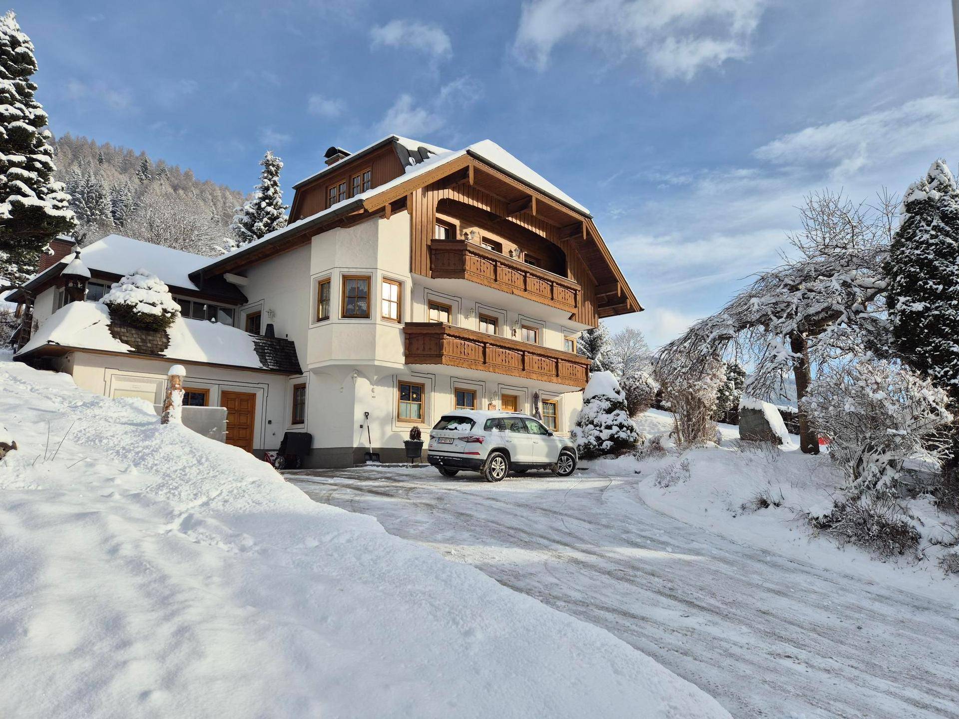 Alpines Haus im Winter mit schneebedecktem Dach und umliegender Landschaft.