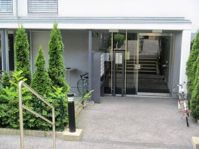 Eingangsbereich eines modernen Wohngebäudes mit Glasfront und gepflegten Pflanzen.