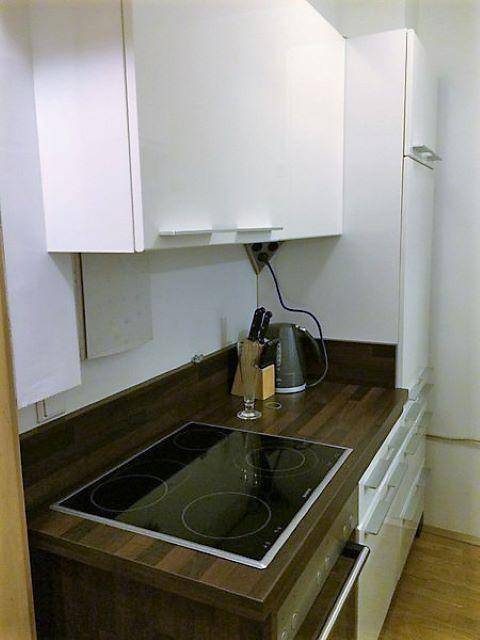 Kleine, moderne Küchenzeile mit dunkler Holz-Arbeitsplatte und weißen Oberschränken.
