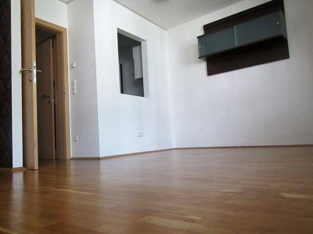Leerer Raum mit glänzendem Holzparkett, einer Tür und einem modernen Wandregal.