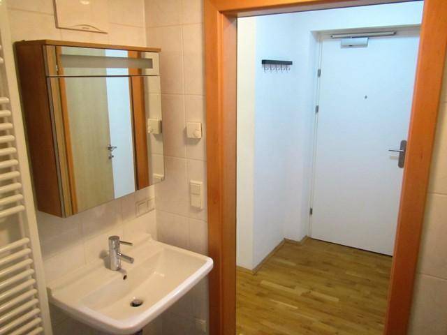 Badezimmer mit Waschbecken, Spiegelschrank und Blick in den angrenzenden Flur.