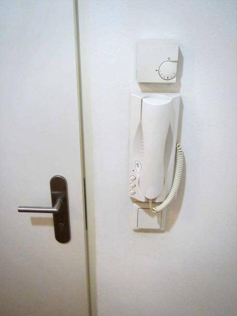 Weiße Gegensprechanlage und Thermostat an einer Wand neben einer Tür.