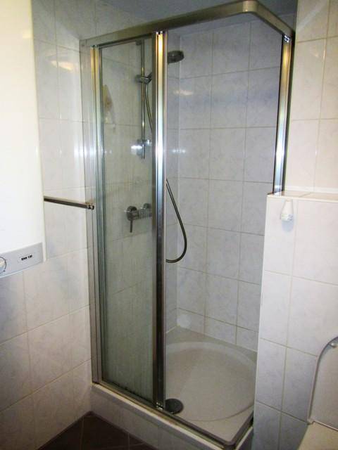 Gefliestes Badezimmer mit einer modernen Duschkabine und weißer Keramik.