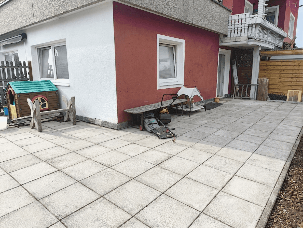Sauberer Terrassenbereich neben dem Haus mit roter Fassade und Kinderspielhaus.
