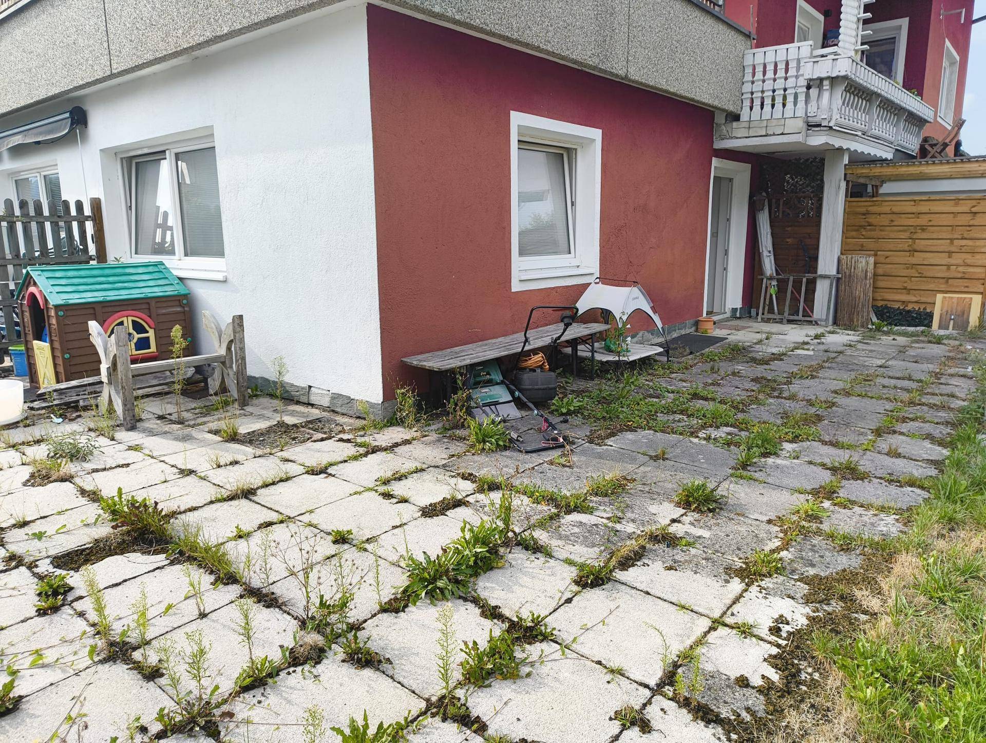 Außenbereich mit roter Fassade, gepflasterter Fläche und einem kleinen Spielhaus für Kinder.