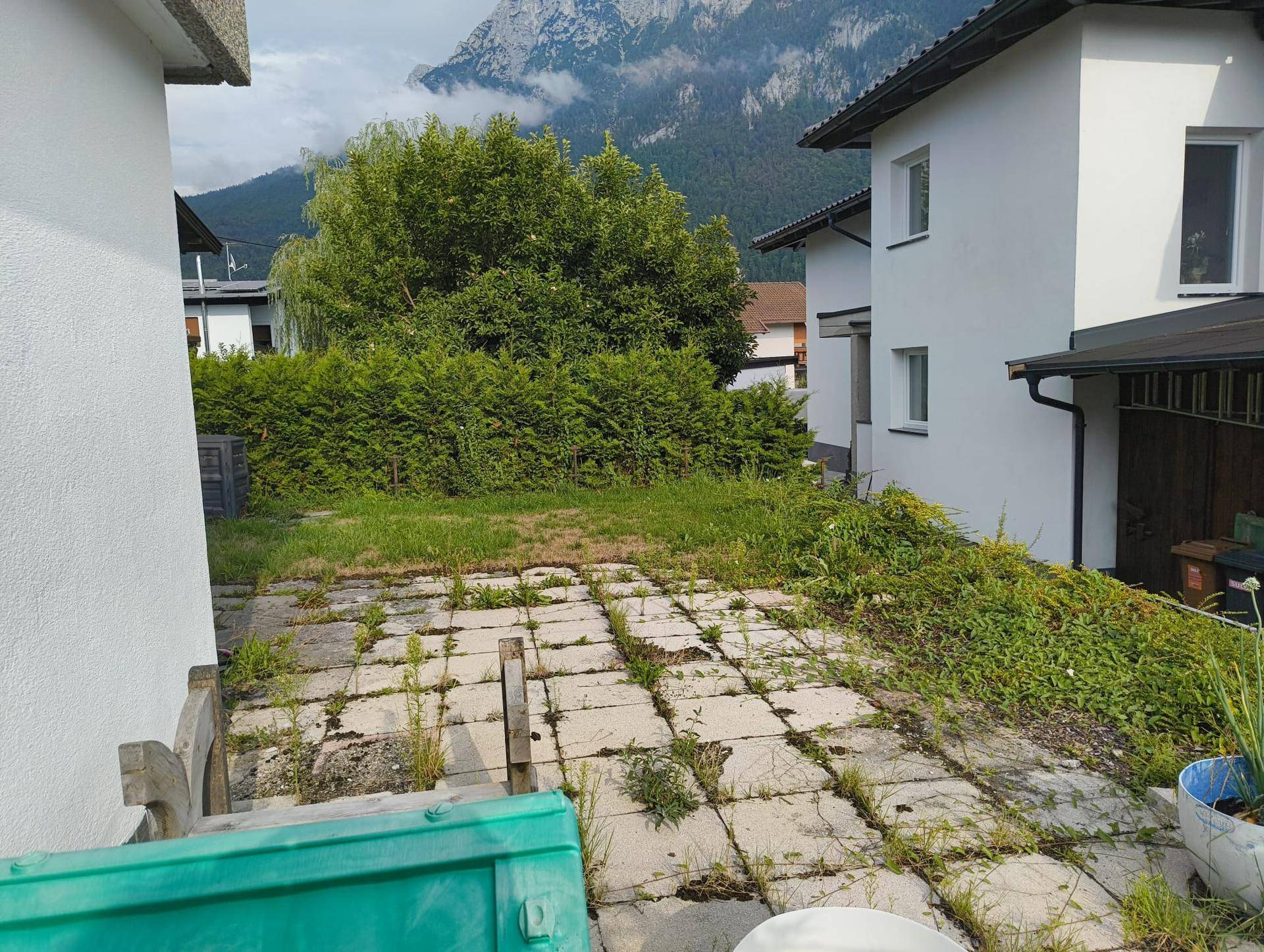 Gartenbereich mit gepflastertem Weg, Hecke und malerischem Bergblick im Hintergrund.