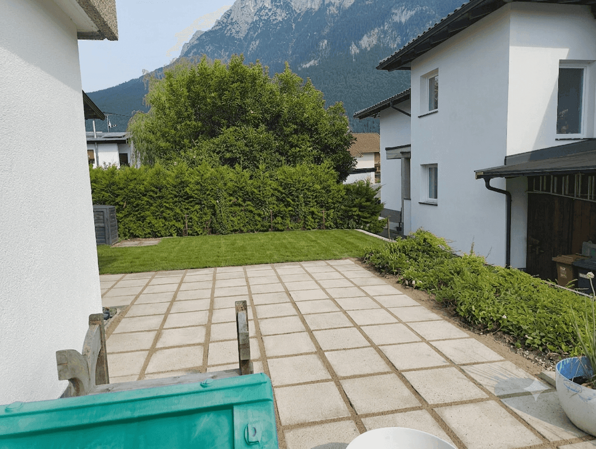 Gepflegter Garten mit Rasenfläche, Hecke und beeindruckendem Bergblick.