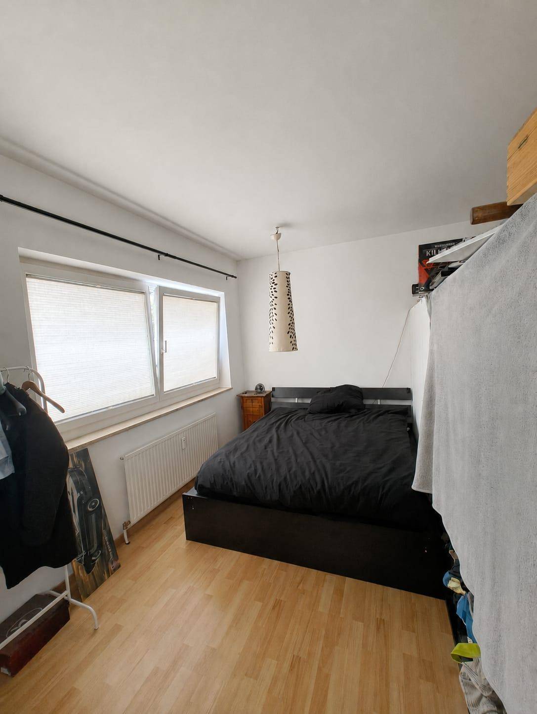Schlafzimmer mit Holzboden, großem Fenster und einfacher, funktionaler Einrichtung.