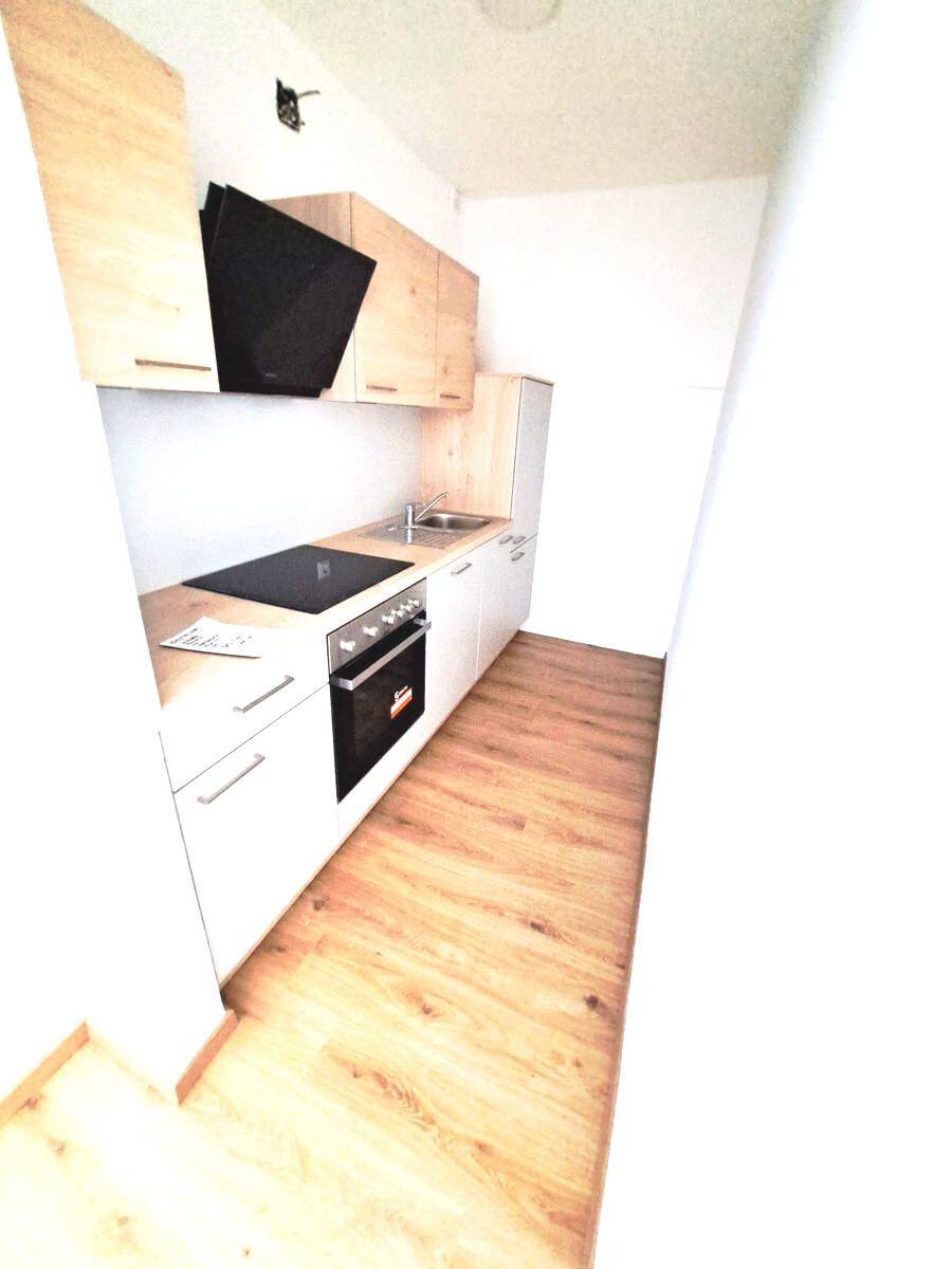 Kompakte Küche mit hellen Holzschränken, Induktionskochfeld, Backofen und Dunstabzugshaube.