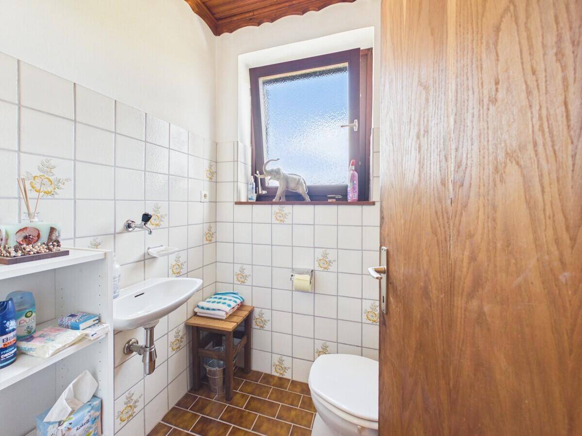 Kleines Gäste-WC mit Fenster, Waschbecken und Toilette, gefliest in Weiß und Braun.