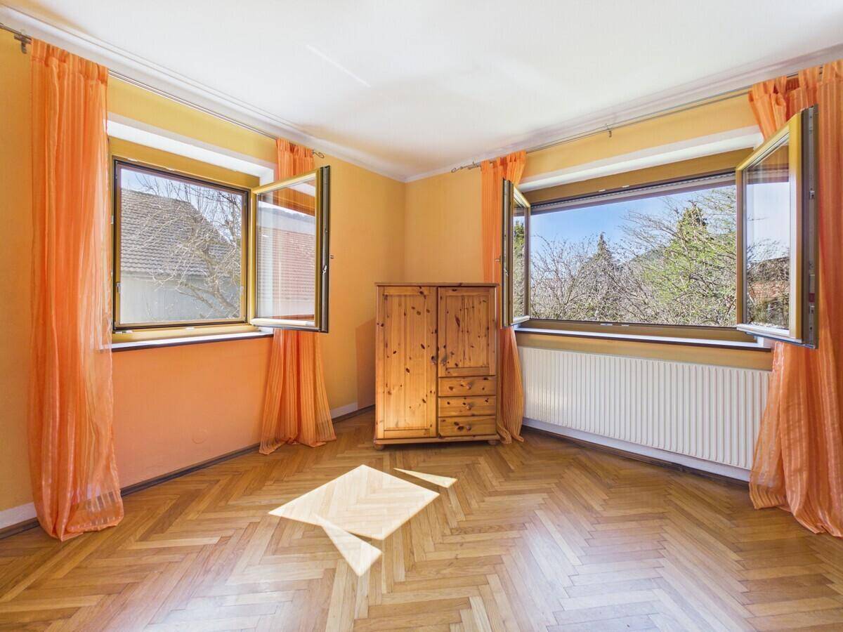Helles Zimmer mit Fischgrätparkett, orangefarbenen Wänden und weitem Blick ins Grüne.