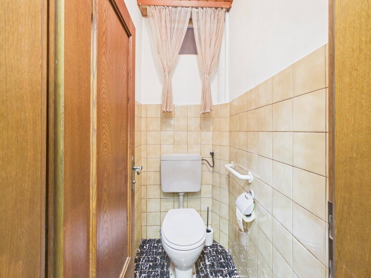 Separate Gästetoilette mit WC, Waschbecken und hellen Fliesen, ausgestattet mit Haltegriffen.