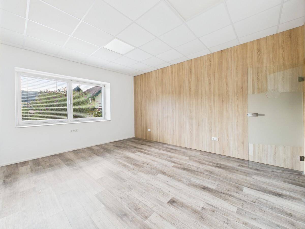Modernes Büro mit Holzwandverkleidung und großem Fenster, das viel Tageslicht hereinlässt.
