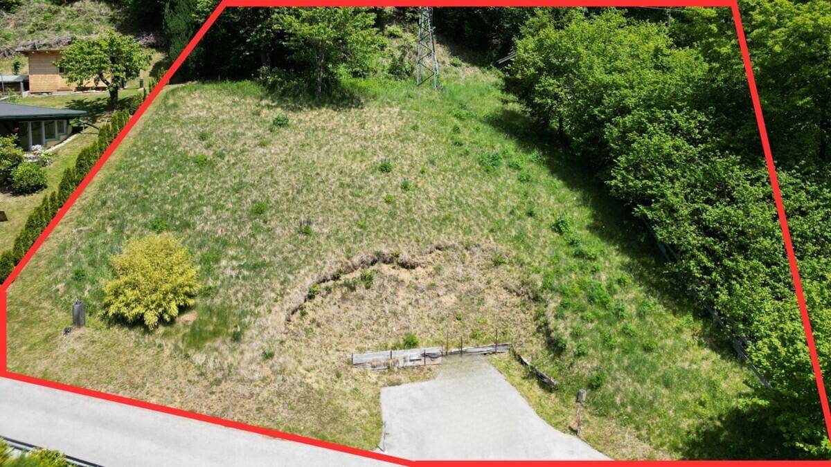 Luftaufnahme eines unbebauten, grasbewachsenen Grundstücks mit roter Umrandung und leichter Hanglage.