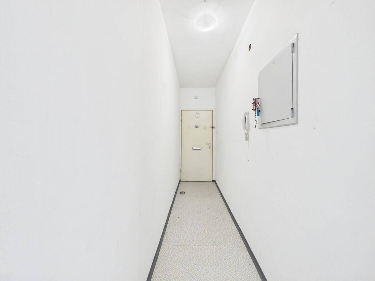 Schmaler, heller Flur mit weiß gestrichenen Wänden und der Eingangstür am Ende.