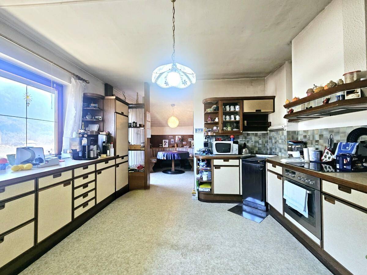 Große Küche mit Essbereich im Hintergrund, vielen Schränken und Geräten.