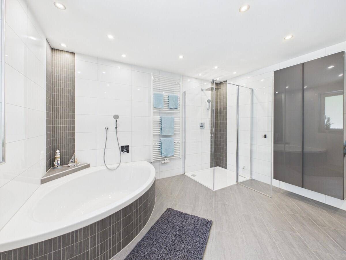 Geräumiges Badezimmer mit moderner Eckbadewanne, großer Dusche und eleganten grauen Schränken.