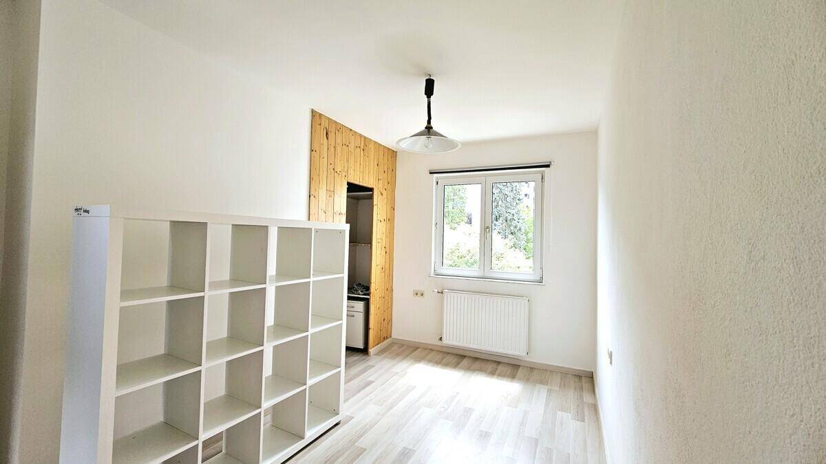 Helles Schlafzimmer mit Laminatboden, Regal und Holzwand mit Schrankbereich.