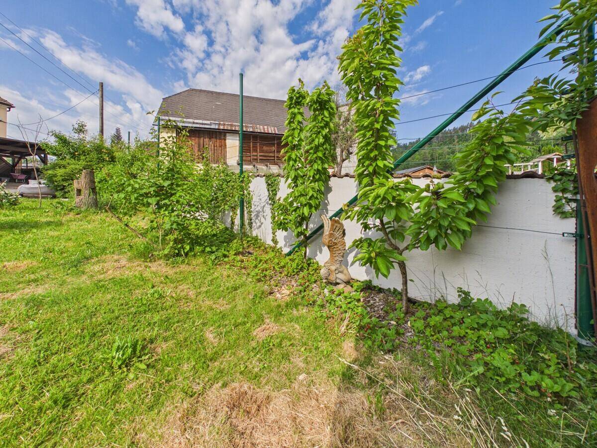 Grüne Rasenfläche mit Büschen und einem Haus im Hintergrund unter blauem Himmel.