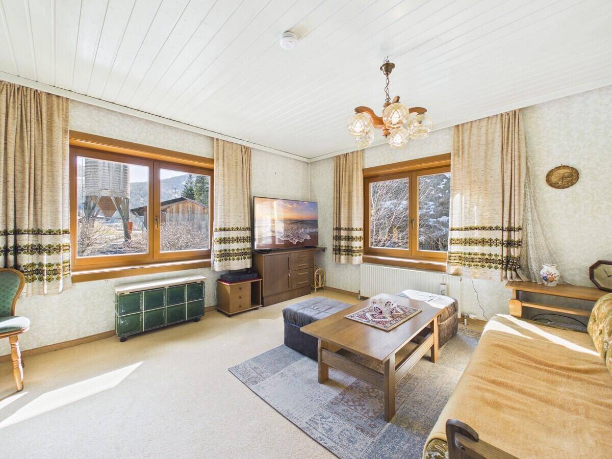 Gemütliches Wohnzimmer mit Teppichboden, Holzdecke und traditioneller Einrichtung.
