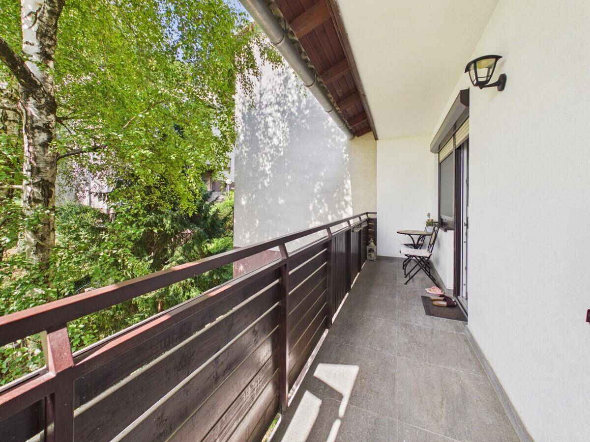 Langer Balkon mit Fliesenboden, Metallgeländer und Blick ins Grüne.