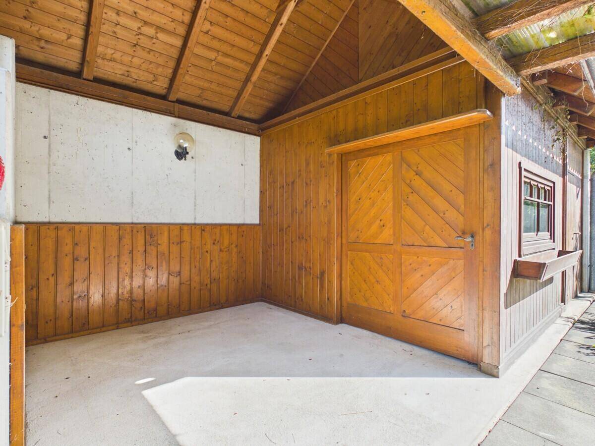 Holzverkleideter Carport mit schrägem Holzdach und Betonboden.