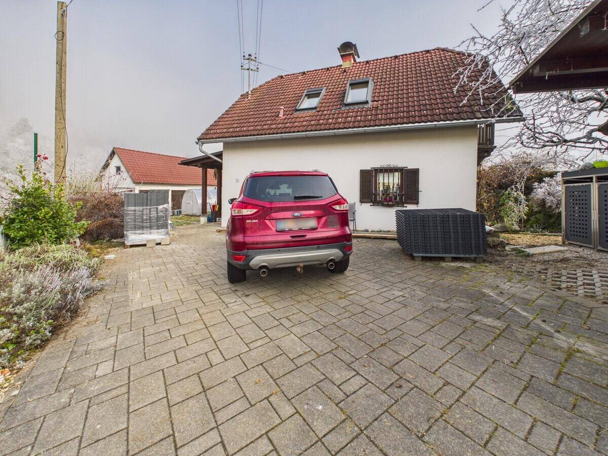 Einfamilienhaus mit gepflasterter Auffahrt und einem geparkten roten Auto davor.