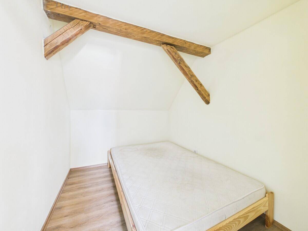 Kleines Schlafzimmer im Dachgeschoss mit einfachem Bettrahmen und sichtbaren Holzbalken.