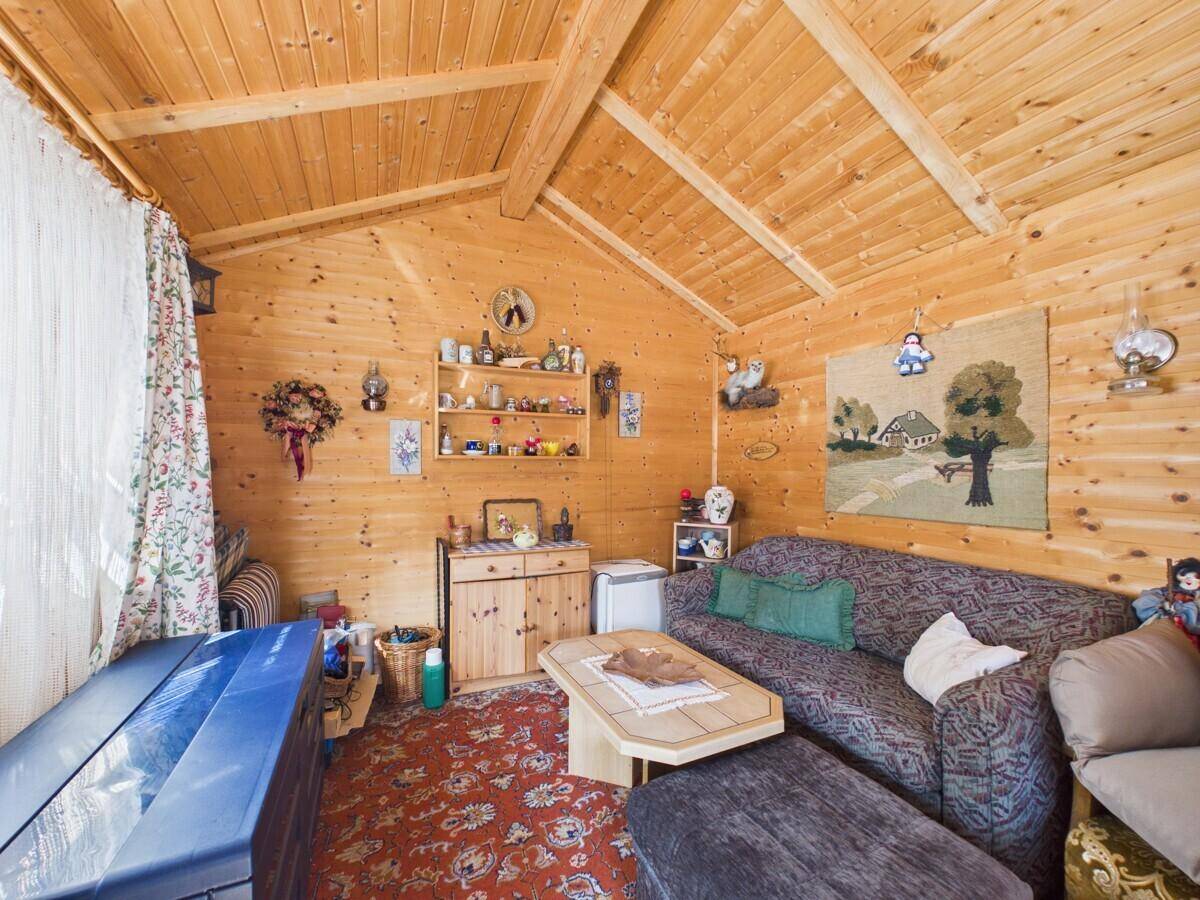 Rustikales Wohnzimmer im Gartenhaus mit Holzvertäfelung, Teppichboden und gemütlicher Sitzecke.