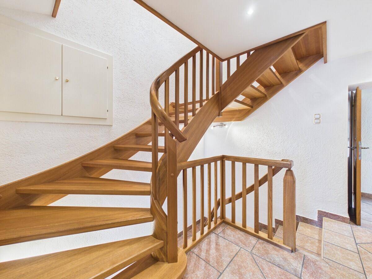 Elegante Holztreppe mit geschwungenem Geländer und gefliestem Boden im Eingangsbereich.