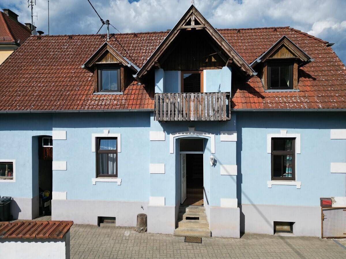 Nahaufnahme der Hausfassade mit blauem Anstrich, rotem Ziegeldach und einem kleinen Holzbalkon.