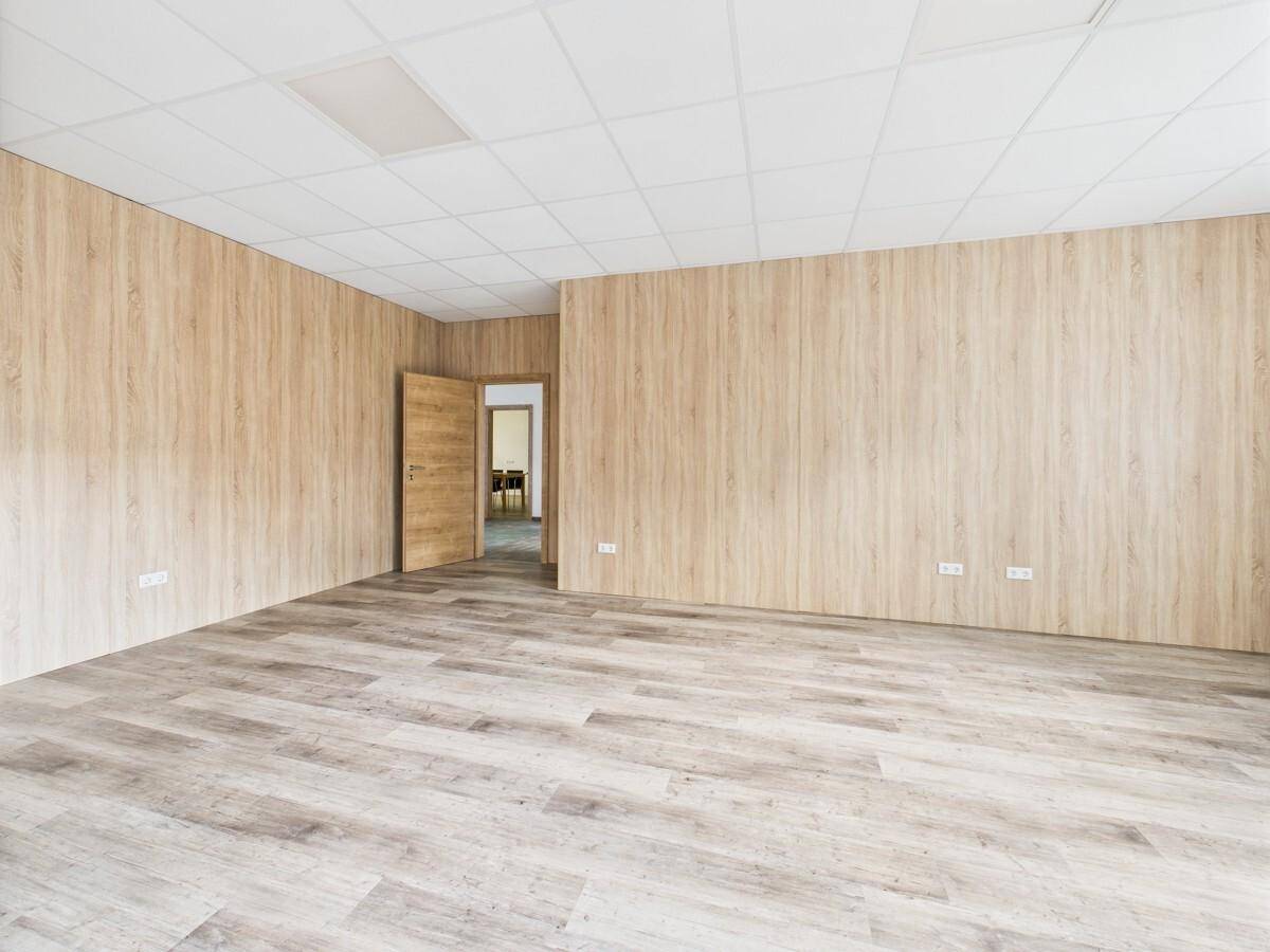Großes Büro mit Holzwandverkleidung und hellem Laminatboden, Tür zu weiteren Räumen.