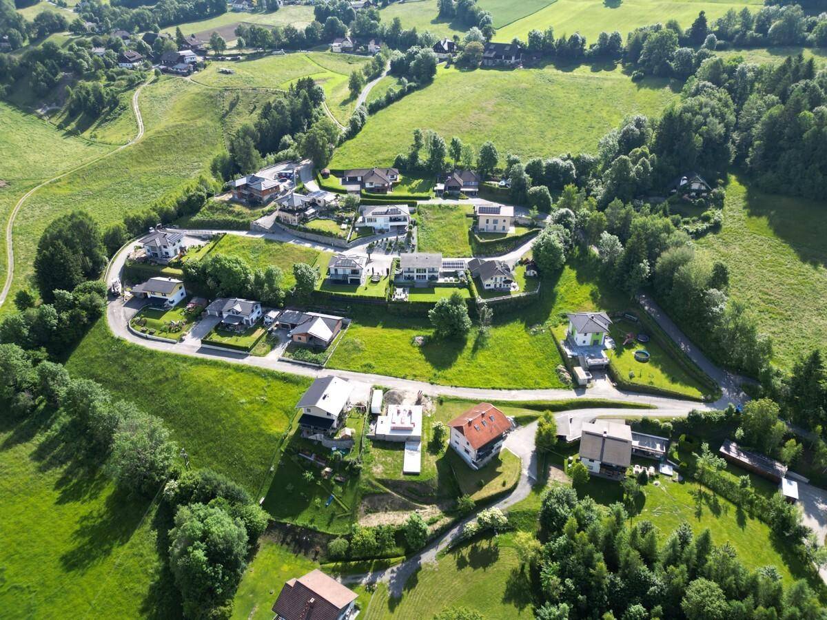 Panoramablick aus der Vogelperspektive auf eine ländliche Wohnsiedlung eingebettet in eine hügelige, grüne Landschaft.