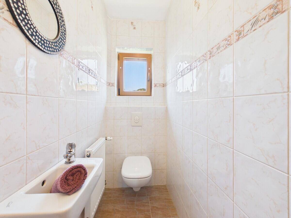 Helles Gäste-WC mit wandhängendem WC, kleinem Waschbecken und Fenster.