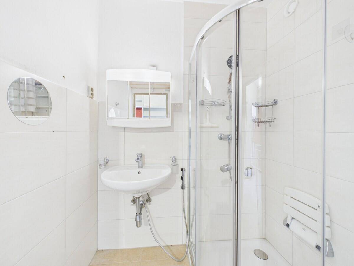 Modernes Badezimmer mit weißen Fliesen, Eckdusche, einzelnen Waschbecken und Haltegriffen.