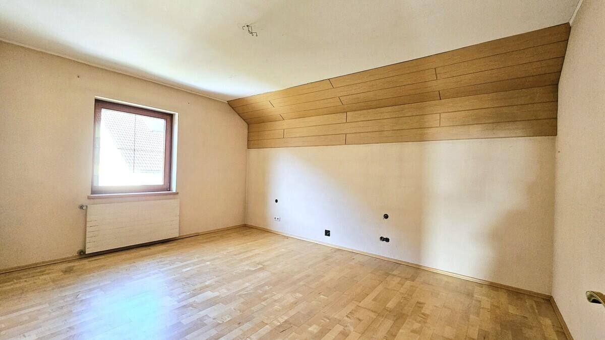 Geräumiges Zimmer mit Holzboden, Dachschräge und Fenster.